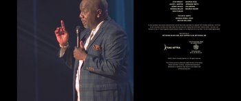 Movie still from “Chappelle's Home Team - Earthquake: Legendary” (2022), directed by Stan Lathan – A man holding a microphone in front of an audience; Extreme Wide shot, Overhead angle