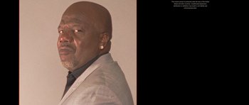 Movie still from “Chappelle's Home Team - Earthquake: Legendary” (2022), directed by Stan Lathan – An older bald man wearing a suit and tie; Extreme Close Up shot, Low angle