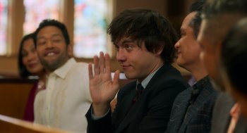 Movie still from “Easter Sunday” (2022), directed by Jay Chandrasekhar – A man in a suit and tie sitting in front of other people; Medium shot, Over the shoulder angle