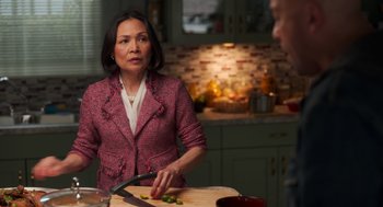 Movie still from “Easter Sunday” (2022), directed by Jay Chandrasekhar – A woman in a pink jacket is cutting food; Medium shot, Over the shoulder angle