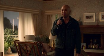 Movie still from “Easter Sunday” (2022), directed by Jay Chandrasekhar – A bald man holding a microphone in a living room; Medium shot, Over the shoulder angle