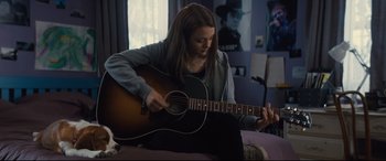 Movie still from “A Dog's Journey” (2019), directed by Gail Mancuso – A woman sitting on a couch playing an acoustic guitar; Medium shot, Over the shoulder angle