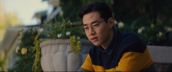 Movie still from “A Dog's Journey” (2019), directed by Gail Mancuso – A young man wearing glasses sitting in front of a flower pot; Close Up shot, Over the shoulder angle