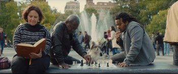 Movie still from “A Dog's Journey” (2019), directed by Gail Mancuso – Two men playing chess in a park with a fountain in the background; Medium shot, Over the shoulder angle