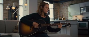 Movie still from “A Dog's Journey” (2019), directed by Gail Mancuso – A woman sitting on a couch playing a guitar; Medium shot, Over the shoulder angle