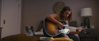 Movie still from “A Dog's Journey” (2019), directed by Gail Mancuso – A woman sitting on top of a bed playing a guitar; Medium shot, Over the shoulder angle