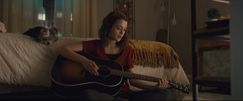 Movie still from “A Dog's Journey” (2019), directed by Gail Mancuso – A woman sitting on a couch playing a guitar; Medium shot, Over the shoulder angle