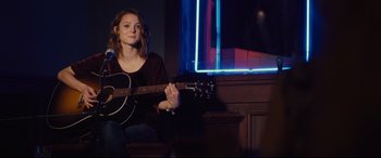 Movie still from “A Dog's Journey” (2019), directed by Gail Mancuso – A woman sitting on a chair holding a guitar; Medium shot, Over the shoulder angle