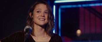 Movie still from “A Dog's Journey” (2019), directed by Gail Mancuso – A young woman smiles brightly while standing in a dark room; Close Up shot, Over the shoulder angle