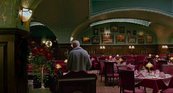 Movie still from “Eastern Promises” (2007), directed by David Cronenberg – A man sitting at a table in front of a bunch of red chairs; Wide shot, Low angle