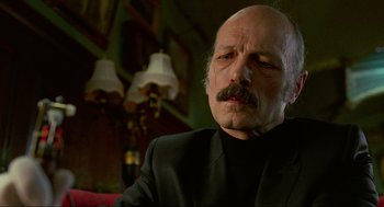 Movie still from “Eastern Promises” (2007), directed by David Cronenberg – An older bald man with a mustache wearing a black suit; Close Up shot, Low angle