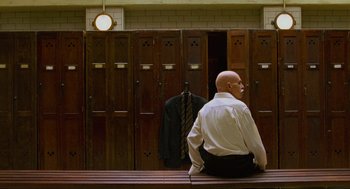 Movie still from “Eastern Promises” (2007), directed by David Cronenberg – A man sitting on top of a wooden bench in front of lockers; Medium shot, Low angle