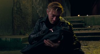 Movie still from “Eastern Promises” (2007), directed by David Cronenberg – A man sitting on the ground holding a bag; Medium shot, High angle
