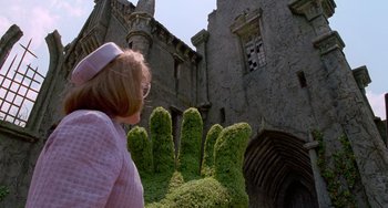Movie still from “Edward Scissorhands” (1990), directed by Tim Burton – A woman standing in front of a building with a giant hand made from bushes; Medium shot, Low angle