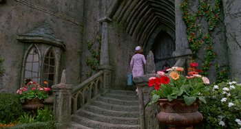 Movie still from “Edward Scissorhands” (1990), directed by Tim Burton – A woman walking down a set of stairs with flowers; Wide shot, Low angle