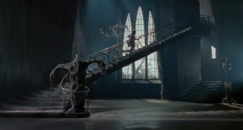 Movie still from “Edward Scissorhands” (1990), directed by Tim Burton – A staircase in a dark room with a statue on it; Extreme Wide shot, High angle