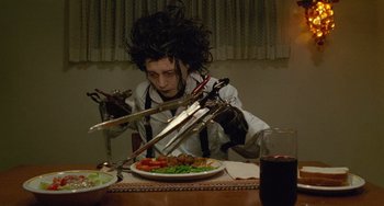 Movie still from “Edward Scissorhands” (1990), directed by Tim Burton – A man sitting at a table with a plate of food; Medium shot, High angle