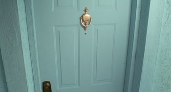 Movie still from “Edward Scissorhands” (1990), directed by Tim Burton – A door with a brass door knocker on it's side; Medium shot, High angle