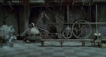 Movie still from “Edward Scissorhands” (1990), directed by Tim Burton – An industrial style room with a bench and a large machine part; Extreme Wide shot, High angle