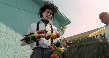 Movie still from “Edward Scissorhands” (1990), directed by Tim Burton – A man in a white shirt and black tie holding a bunch of food; Medium shot, Low angle