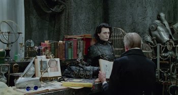 Movie still from “Edward Scissorhands” (1990), directed by Tim Burton – A woman sitting in front of a table full of books; Medium shot, Over the shoulder angle