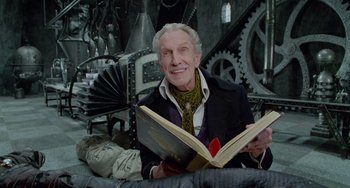 Movie still from “Edward Scissorhands” (1990), directed by Tim Burton – An older man sitting on a couch reading a book; Medium shot, Low angle