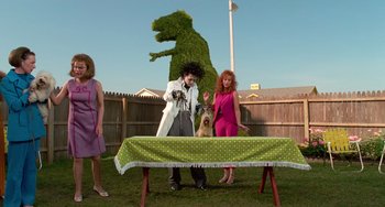 Movie still from “Edward Scissorhands” (1990), directed by Tim Burton – Two women and a man with a dog on a table in a yard; Wide shot, Low angle
