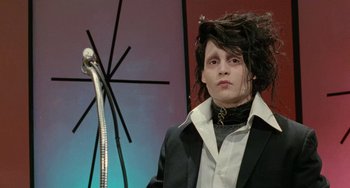 Movie still from “Edward Scissorhands” (1990), directed by Tim Burton – A young man with long black hair is posing for a picture; Medium shot, Low angle