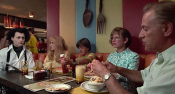 Movie still from “Edward Scissorhands” (1990), directed by Tim Burton – Three people sitting at a table with plates of food in front of them; Medium shot, Over the shoulder angle