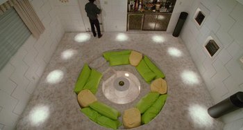 Movie still from “Edward Scissorhands” (1990), directed by Tim Burton – A man standing next to a room with green pillows on the floor; Extreme Wide shot, Overhead angle