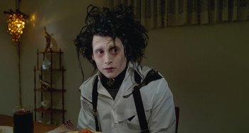 Movie still from “Edward Scissorhands” (1990), directed by Tim Burton – A man with a long black hair sitting at a dinner table; Medium shot, Low angle