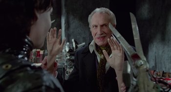 Movie still from “Edward Scissorhands” (1990), directed by Tim Burton – An older man in a suit and tie holding a pair of scissors in front of a mirror; Medium shot, Over the shoulder angle