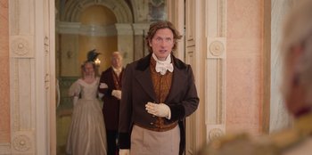 Movie still from “Ehrengard: The Art of Seduction” (2023), directed by Bille August – A man dressed in period clothing standing in front of two other people; Medium shot, Over the shoulder angle