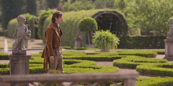 Movie still from “Ehrengard: The Art of Seduction” (2023), directed by Bille August – A man standing in the middle of a lush green garden; Wide shot, Over the shoulder angle