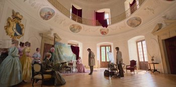 Movie still from “Ehrengard: The Art of Seduction” (2023), directed by Bille August – A group of people in a room with paintings on the walls; Wide shot, Low angle