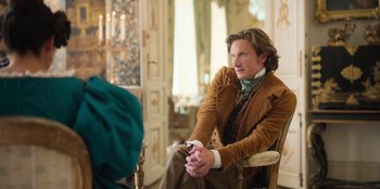 Movie still from “Ehrengard: The Art of Seduction” (2023), directed by Bille August – A man sitting in a chair in front of a mirror; Medium shot, Over the shoulder angle