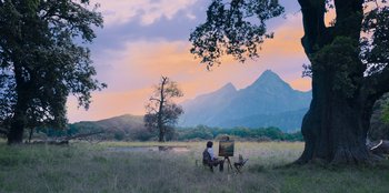 Movie still from “Ehrengard: The Art of Seduction” (2023), directed by Bille August – A person sitting in a field painting a picture; Extreme Wide shot, Low angle
