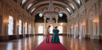 Movie still from “Ehrengard: The Art of Seduction” (2023), directed by Bille August – A man and a woman standing on a red carpet in front of a chandelier; Wide shot, Low angle
