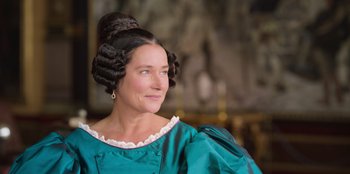 Movie still from “Ehrengard: The Art of Seduction” (2023), directed by Bille August – A woman in a green dress with a black wig; Close Up shot, High angle