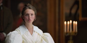 Movie still from “Ehrengard: The Art of Seduction” (2023), directed by Bille August – A woman in a white dress standing in front of a candle; Close Up shot, Low angle