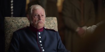 Movie still from “Ehrengard: The Art of Seduction” (2023), directed by Bille August – An older man in a uniform sitting in a chair; Close Up shot, Over the shoulder angle