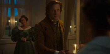 Movie still from “Ehrengard: The Art of Seduction” (2023), directed by Bille August – A man in a brown jacket standing next to a candle; Medium shot, Over the shoulder angle