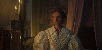 Movie still from “Ehrengard: The Art of Seduction” (2023), directed by Bille August – A woman in a white dress standing next to a window; Medium shot, Low angle