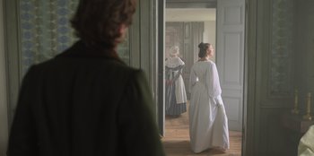 Movie still from “Ehrengard: The Art of Seduction” (2023), directed by Bille August – Two women dressed in period clothing walk through a doorway; Wide shot, Over the shoulder angle