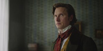 Movie still from “Ehrengard: The Art of Seduction” (2023), directed by Bille August – A man with a red scarf is standing in a room; Close Up shot, Low angle