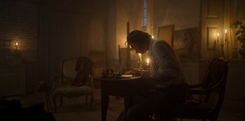Movie still from “Ehrengard: The Art of Seduction” (2023), directed by Bille August – A person sitting at a table writing on a piece of paper; Wide shot, Low angle