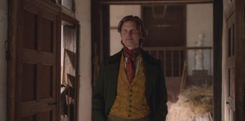 Movie still from “Ehrengard: The Art of Seduction” (2023), directed by Bille August – A man wearing a green jacket standing in a room; Medium shot, Over the shoulder angle
