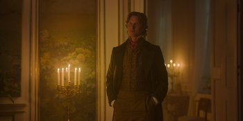 Movie still from “Ehrengard: The Art of Seduction” (2023), directed by Bille August – A man standing in front of candles in a room; Medium shot, Over the shoulder angle