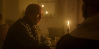 Movie still from “Ehrengard: The Art of Seduction” (2023), directed by Bille August – A man sitting in front of a candle in a dimly - lit room; Close Up shot, Over the shoulder angle