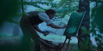Movie still from “Ehrengard: The Art of Seduction” (2023), directed by Bille August – A man painting a picture in the woods; Medium shot, Over the shoulder angle